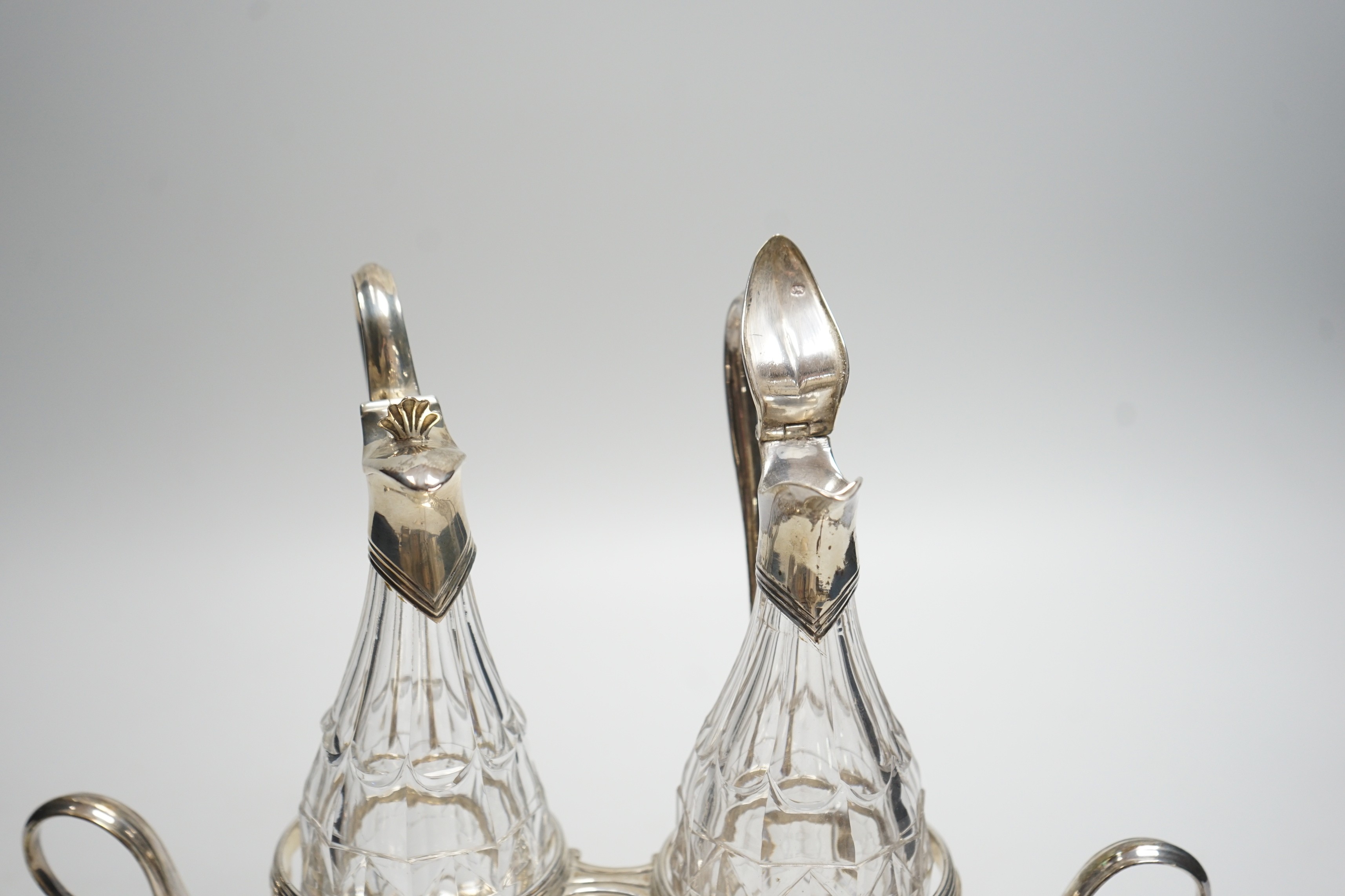 A George III silver navette shaped two handled oil and vinegar stand, with two matching silver mounted cut glass bottles (one thumbpiece missing), John Scofield, London, 1787, length 28cm, stand, 13.7oz.